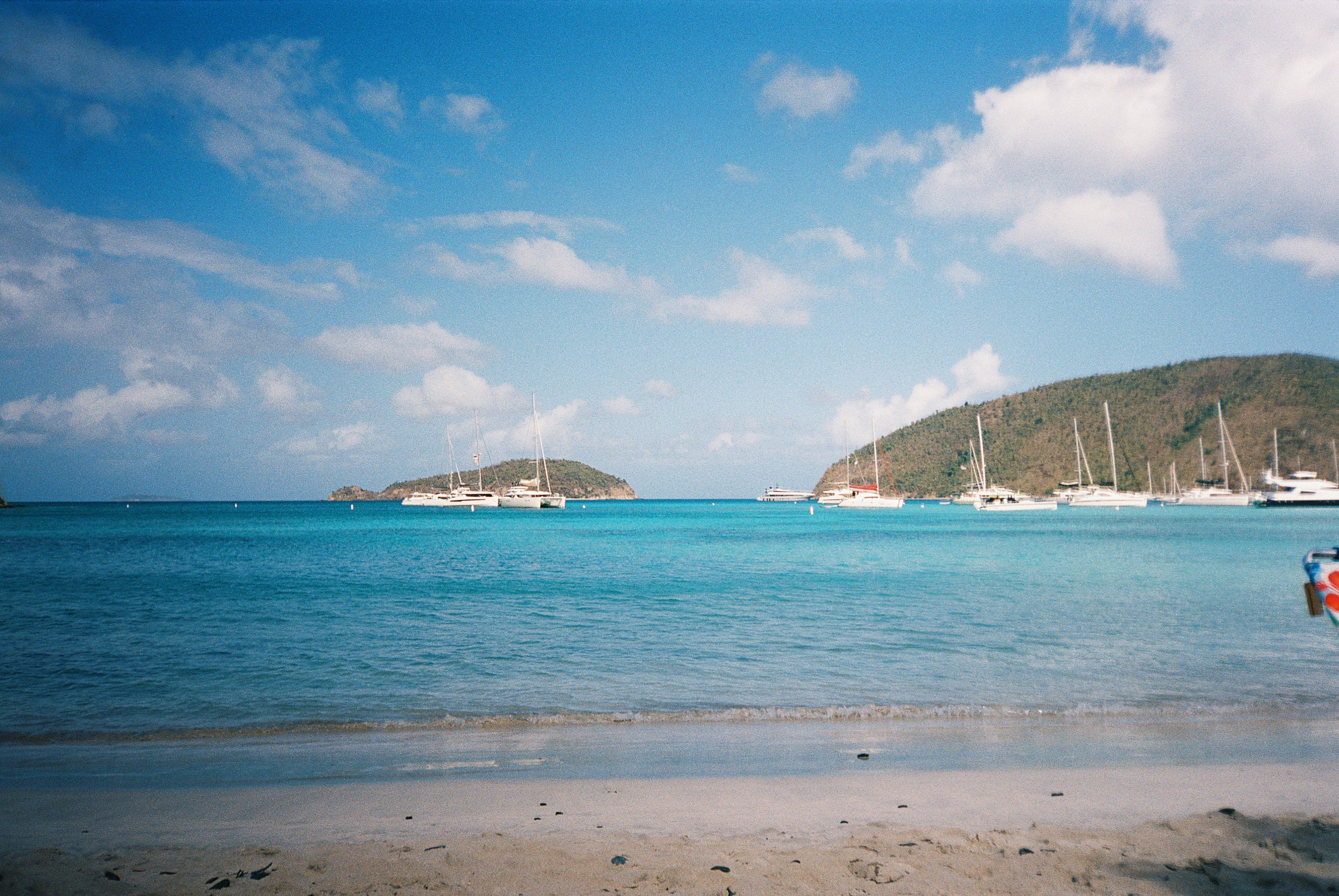 Caribbean beach with sailboats and islands under a sunny sky