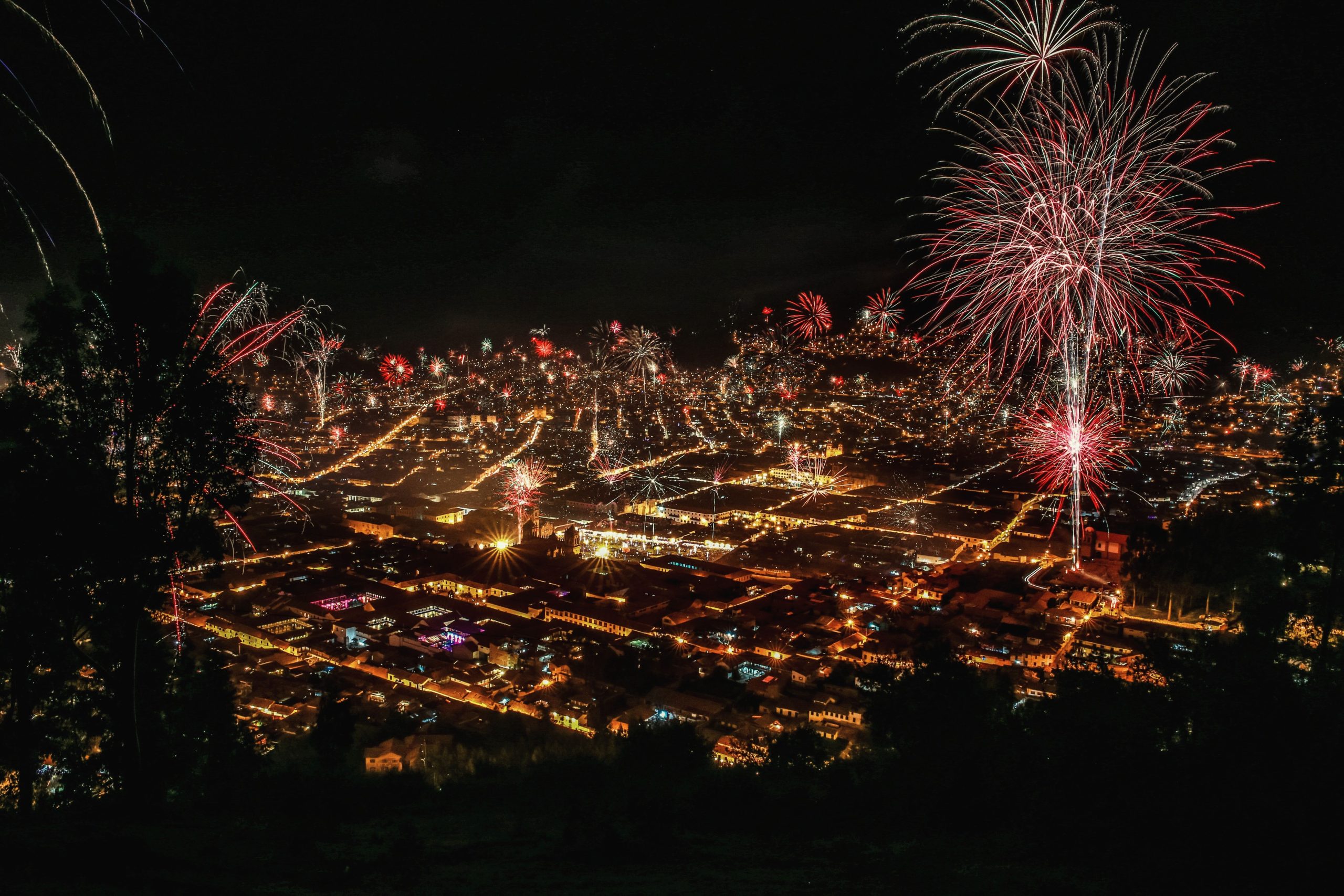 Aerial view of a city skyline lit up by vibrant New Year's Eve fireworks over the water